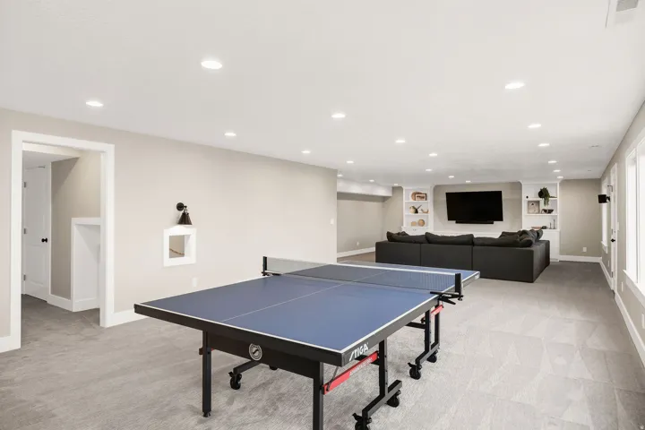 Spacious lower-level area featuring recessed lighting, light gray carpeting, neutral wall tones, and built-in shelving surrounding a media wall