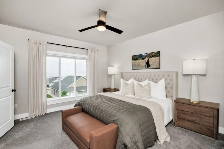 Spacious bedroom featuring light gray walls, large window with white trim, dark wood-finish nightstands, and a contemporary ceiling fan