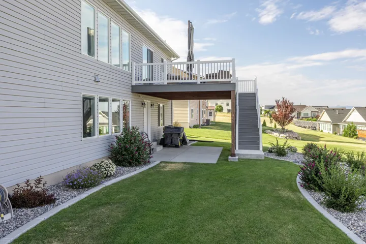 Rear exterior featuring a spacious deck with white railings and stairs, a concrete patio, and a manicured lawn