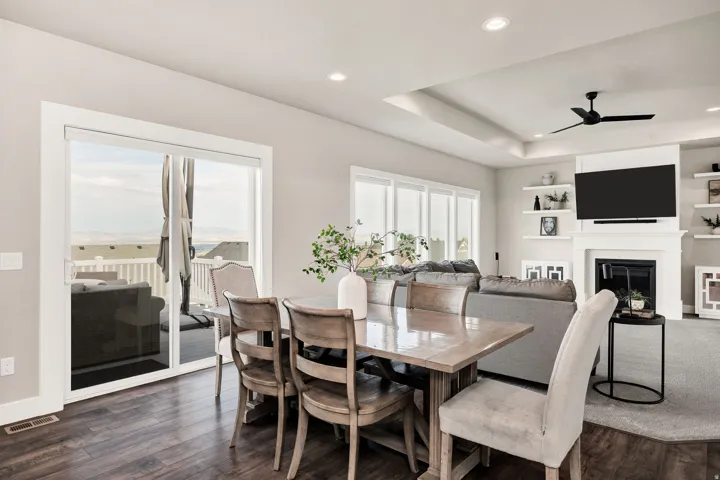 Open-concept living space featuring wood-finish flooring, a contemporary fireplace with mantel, recessed lighting, a tray ceiling, and sliding glass doors leading to an outdoor deck