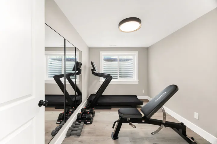Dedicated fitness space featuring a full-wall mirror, two windows, wood-finish flooring, and a modern flush-mount ceiling light