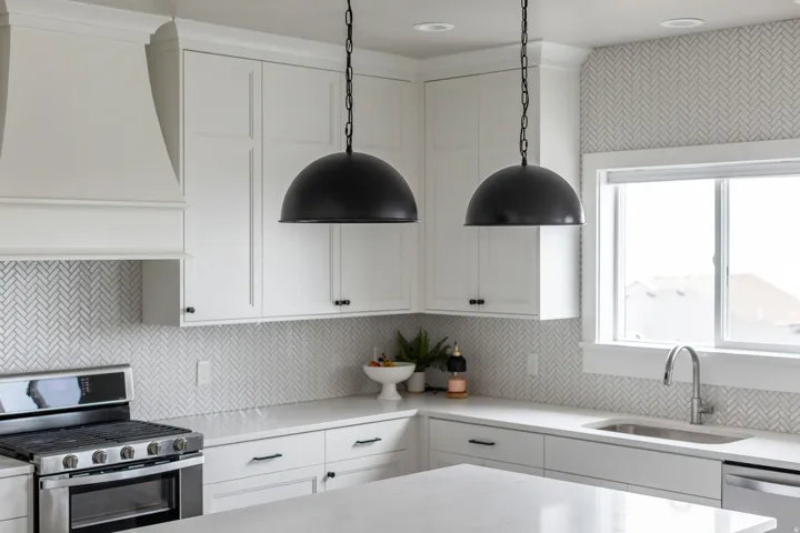 Modern kitchen featuring white shaker cabinetry, stainless steel appliances, a herringbone tile backsplash, and two matte black dome pendant lights