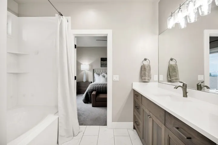 Bathroom featuring a wood-finish vanity with a single sink, light countertop, and a large mirror with overhead lighting