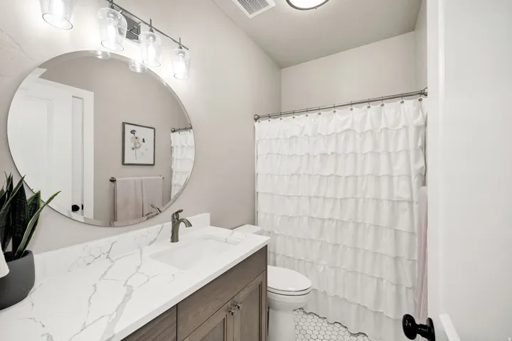 Bathroom featuring a single vanity with wood-finish cabinetry, a white countertop with grey veining, and a circular mirror