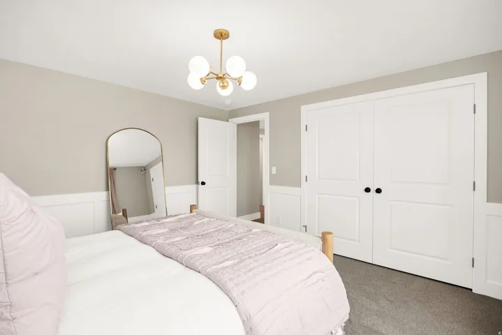 Bedroom featuring a modern gold-finish chandelier, neutral wall paint, white wainscoting, and gray carpeting