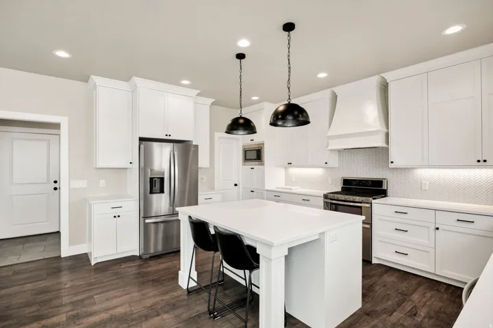 Kitchen featuring a large central island with seating, white shaker-style cabinetry, stainless steel appliances, herringbone pattern tile backsplash, and wood-finish flooring