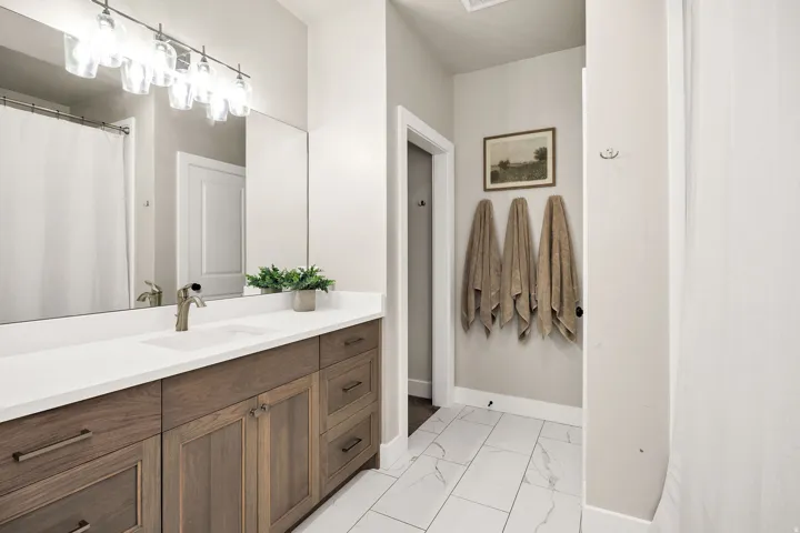 Well-appointed bathroom featuring a spacious wood-finish vanity with a white countertop and integrated sink, brushed nickel faucet, large mirror, and multi-light vanity fixture