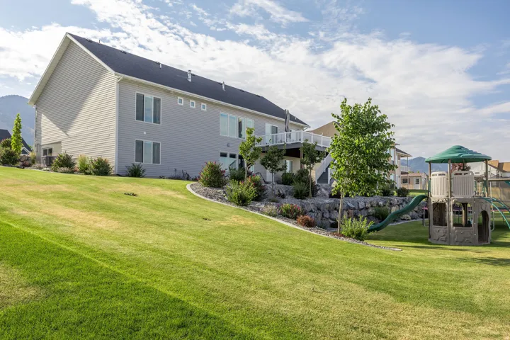 Spacious sloped lawn featuring mature landscaping, a rock retaining wall, and a raised white deck