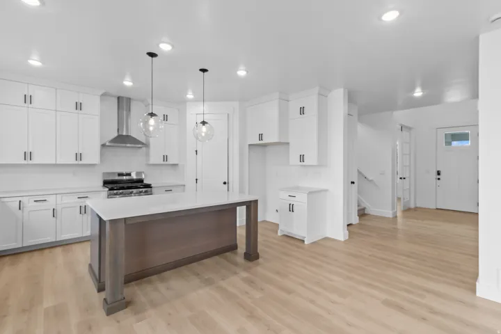 Kitchen featuring a central island with a light-toned countertop, white cabinetry with dark hardware, stainless steel range with overhead ventilation, two suspended globe pendant lights, and wood-finish flooring