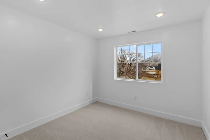 Bright room featuring a large window with muntins, recessed lighting, neutral carpeting, and white baseboards