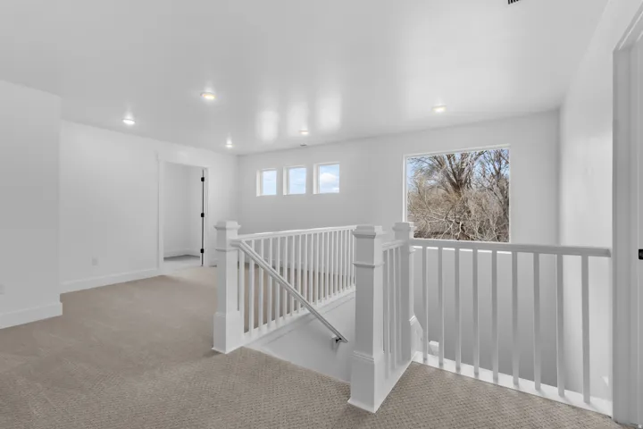 Open landing area featuring neutral carpet flooring, recessed lighting, white trim, and multiple windows