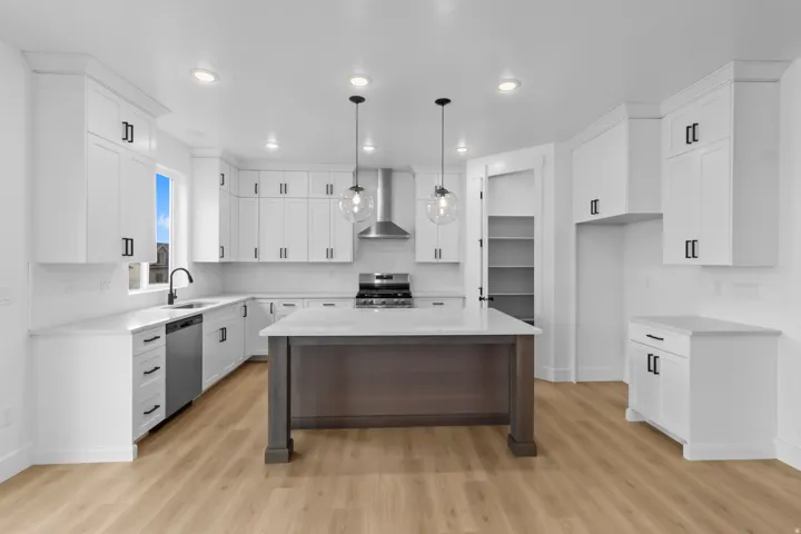 Modern kitchen featuring a central island with a light-toned countertop, white cabinetry with black hardware, stainless steel appliances, wood-finish flooring, and recessed and pendant lighting
