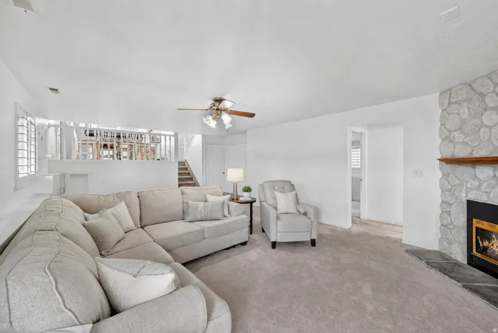 Living area featuring a stone-clad fireplace with a wood mantel, light-toned carpet flooring, and white painted walls