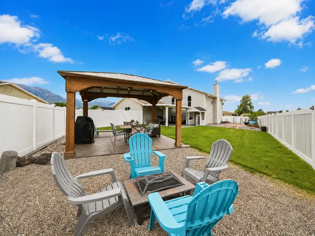 Outdoor living area featuring a wood-frame gazebo with a metal roof, a gravel fire pit area, a concrete patio, a manicured lawn, and a white privacy fence
