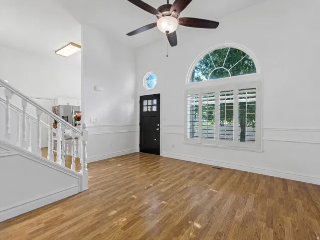 Vaulted ceiling entry featuring wood-finish flooring, a decorative arched window with plantation shutters, and a ceiling fan with light fixture