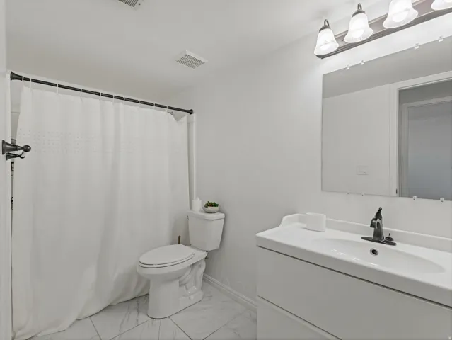Bathroom featuring a white vanity with integrated sink, a rectangular mirror, and a wall-mounted light fixture