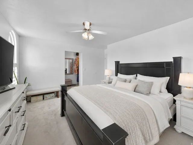 Bedroom featuring wall-to-wall carpeting, an arched window with louvered shutters, and a ceiling fan with integrated lighting