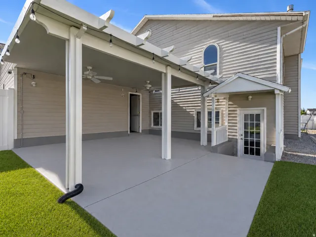 Expansive covered patio featuring a pergola with string lighting, multiple ceiling fans, and a direct entry door