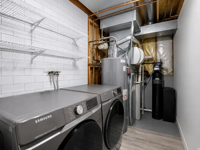 Dedicated laundry area featuring wire shelving, subway tile wall, water heater, and wood-finish flooring