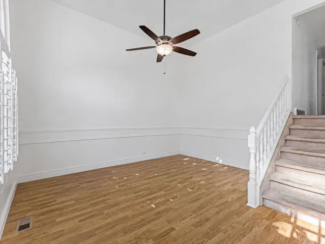 Room featuring wood-finish flooring, white wall paneling, a ceiling fan with integrated lighting, and a staircase with a white baluster and carpeted treads