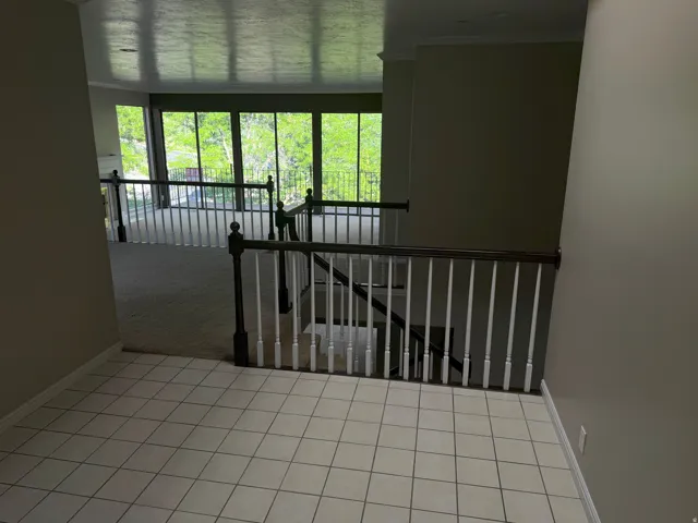 Open concept interior featuring tile flooring, carpeted areas, white baluster railings with dark wood top rails, and a wall of windows