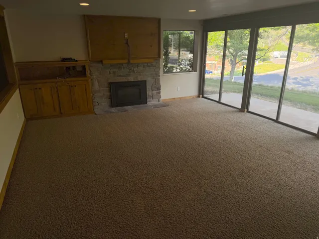 Carpeted living area featuring a stone-faced fireplace with a black insert, built-in wooden cabinetry, a wooden mantel, recessed lighting, and large sliding glass doors
