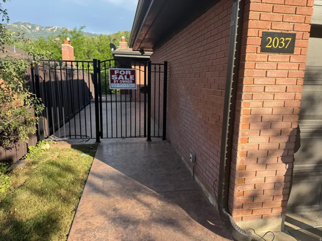 Brick exterior with an elegant black iron gate, stamped concrete pathway, and an address plaque