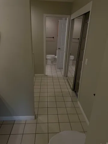 Tiled flooring throughout this hallway bathroom, featuring two distinct toilet areas, two white doors, and a mirrored closet door