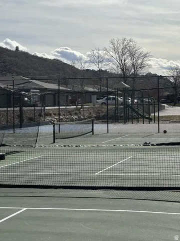 Tennis court with a green surface and white line markings, secured by dark fencing