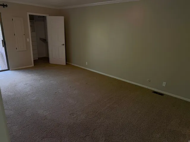 Carpeted room featuring a sliding glass door, a built-in closet with shelving, a two-panel interior door, baseboard molding, and crown molding