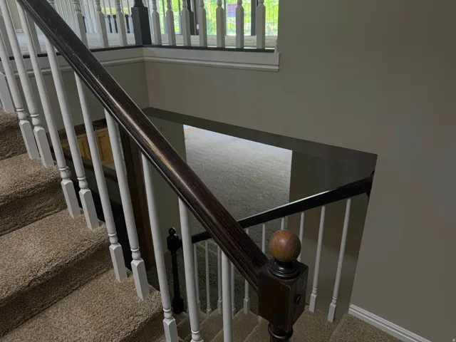 Staircase with carpeted treads and risers, featuring a dark wood handrail, white balusters, and a decorative newel post