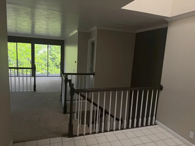 Upper-level landing featuring a white tiled entry, dark wood railing with white balusters, and crown molding