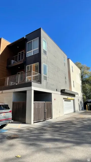 Modern multi-story building featuring a stucco facade, multiple balconies with metal railings, and a ground-level garage door