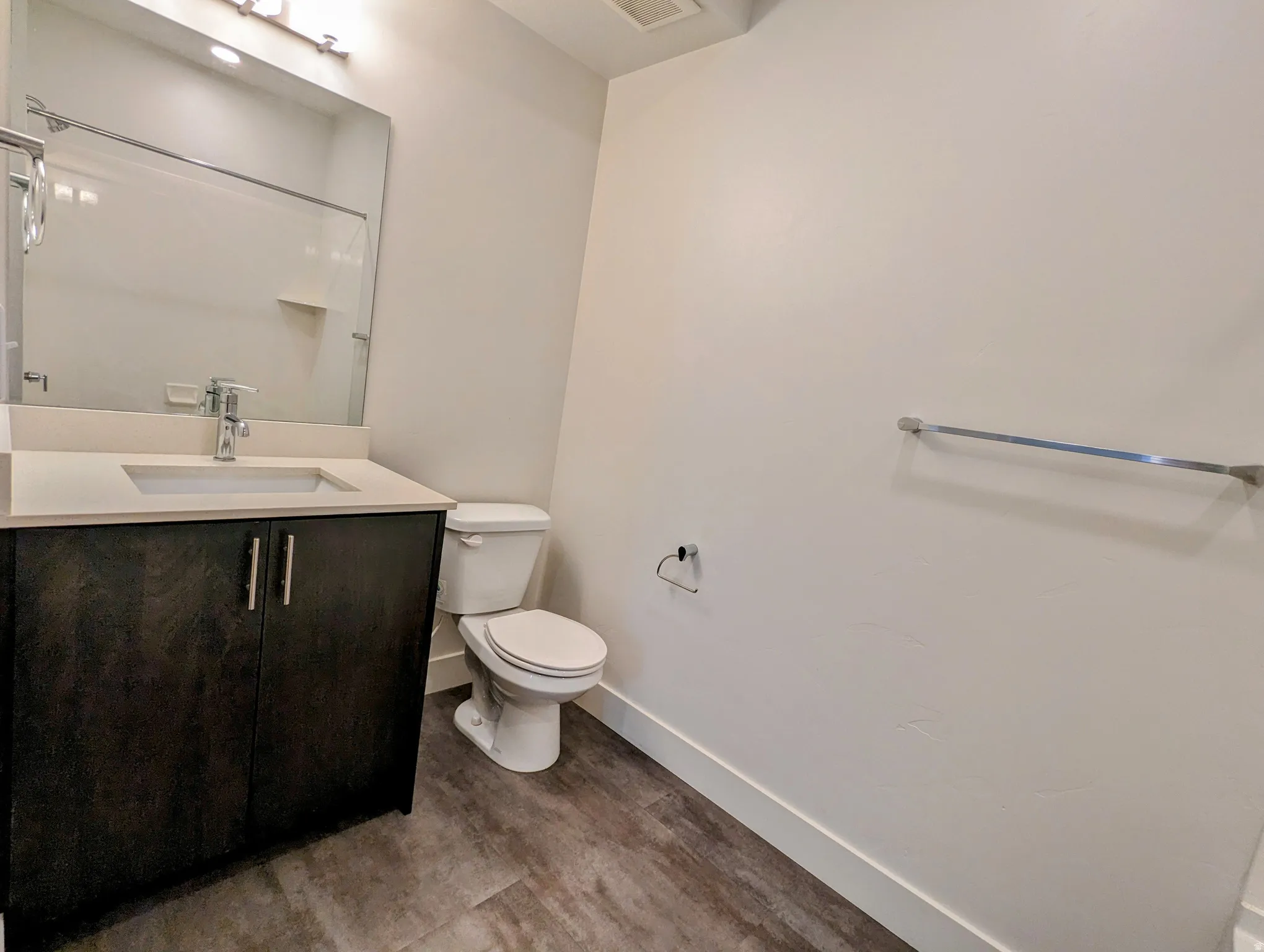 Bathroom featuring a dark wood-finish vanity with a light countertop and integrated sink, a large wall-mounted mirror, and wood-look flooring