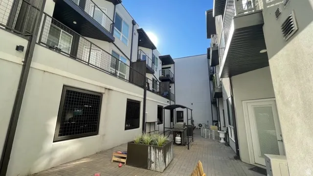 Paved exterior courtyard featuring a textured planter with greenery, ground-level window grilles, and upper-level balconies with metal railings