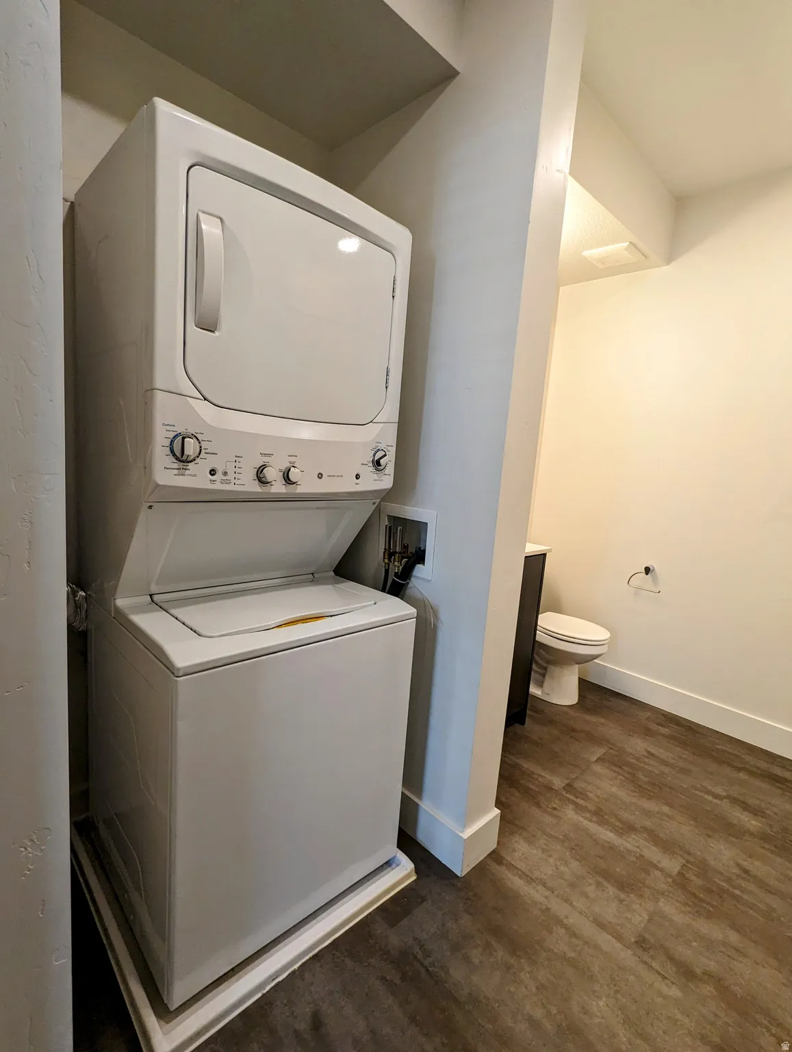 Dedicated laundry area featuring a white stacked washer and dryer, wood-finish flooring, and white baseboards
