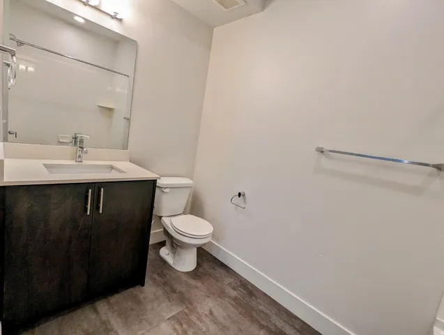 Bathroom featuring a dark wood-finish vanity with a light countertop and integrated sink, a large wall-mounted mirror, and wood-look flooring