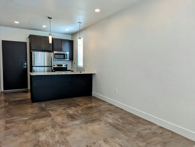 Open-concept kitchen featuring dark wood cabinetry, stainless steel appliances, a breakfast bar with a light-toned countertop, and modern pendant lighting