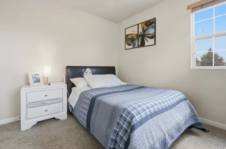 Carpeted room featuring a white-framed window, neutral painted walls, white baseboards, and a black headboard