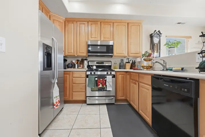Kitchen featuring light wood cabinetry, white countertops, stainless steel refrigerator, stainless steel range with overhead microwave, and a black dishwasher