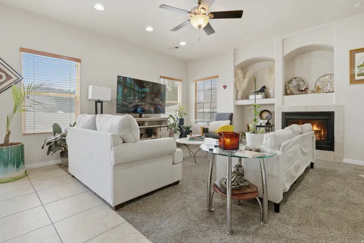 Living area featuring a fireplace with a tile surround, built-in display niches, recessed lighting, a ceiling fan, and a combination of tile and carpet flooring