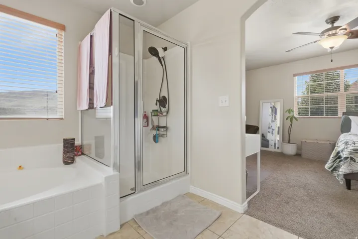 Bathroom featuring a glass-enclosed shower with a dark bronze fixture, a white tiled soaking tub, and tan tile flooring