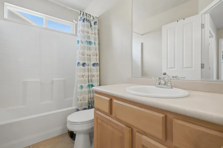 Bathroom featuring a light wood-finish vanity with an integrated sink, a large wall-mounted mirror, and a white tub with tile-effect surround