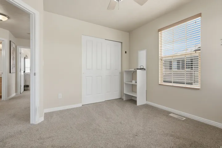 Neutral-toned room featuring light beige wall paint, plush carpeting, a window with horizontal blinds, and a ceiling fan