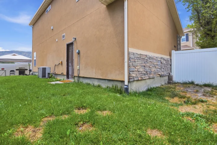 Rear exterior featuring stucco siding, stone veneer accents, and a white vinyl fence