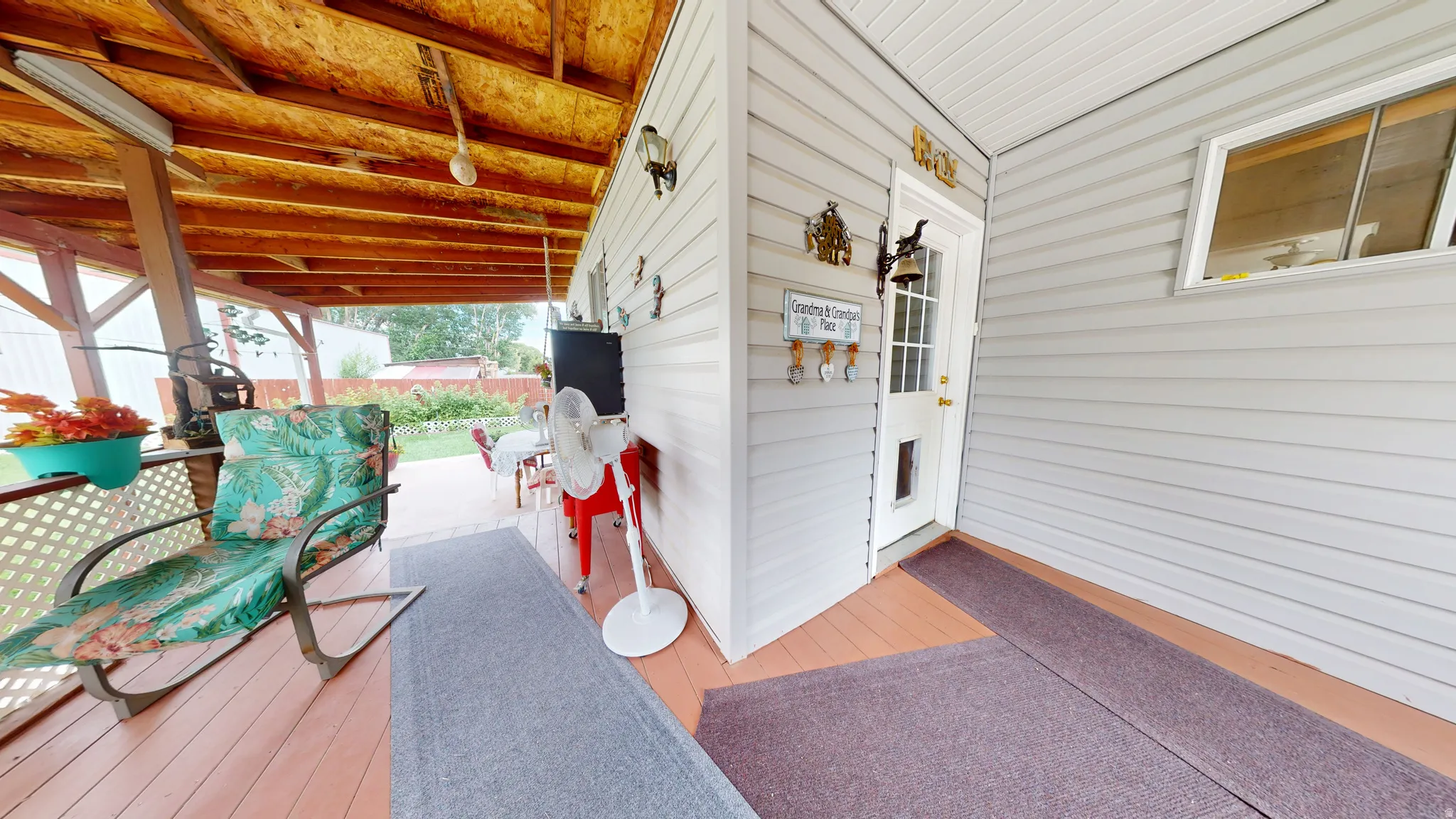 Covered porch with wood-finish flooring, exposed beam ceiling, white lattice railing, and light gray siding