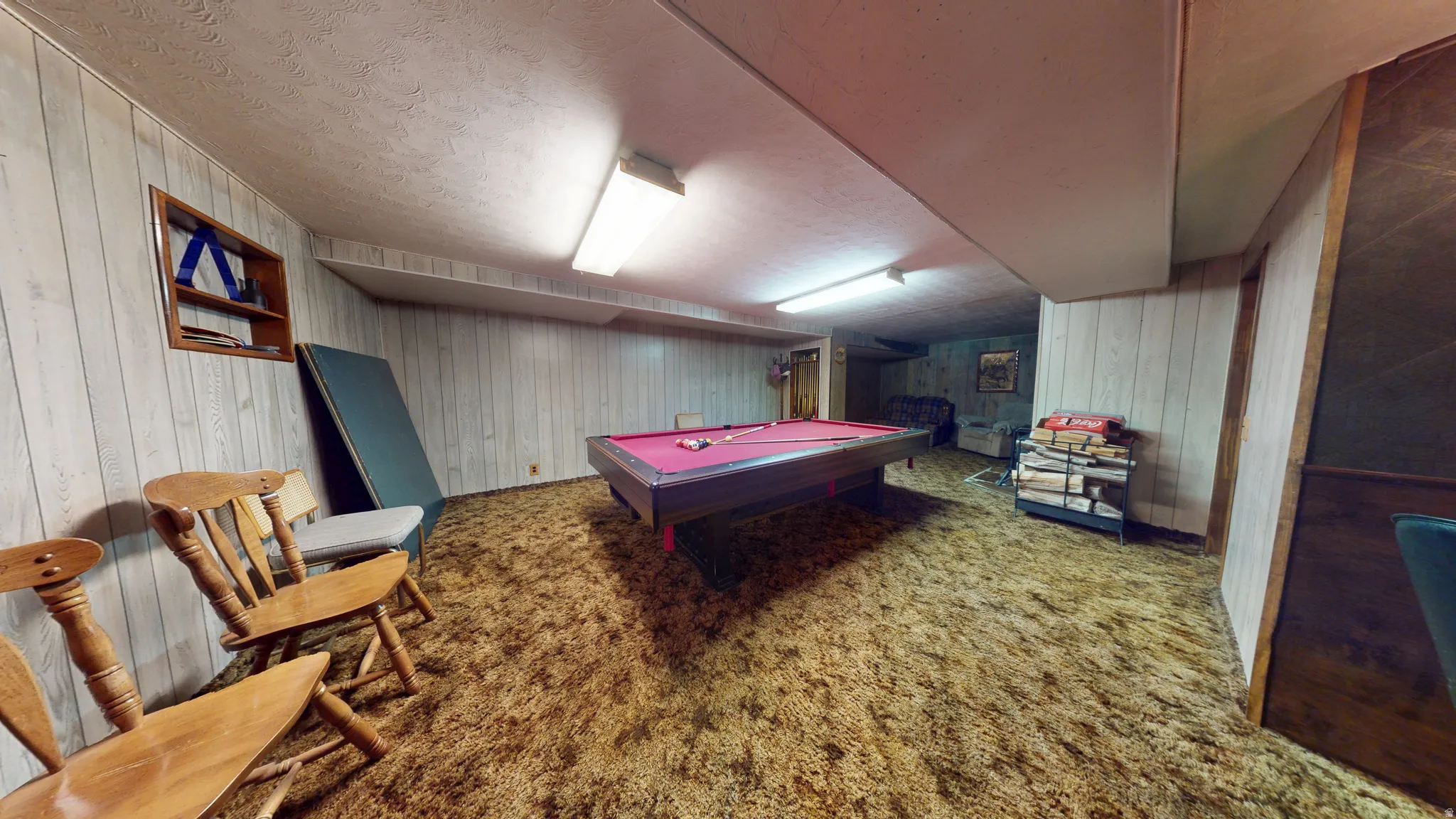 Recreation room featuring a pool table with red felt, wood paneling, and wall-mounted fluorescent lighting