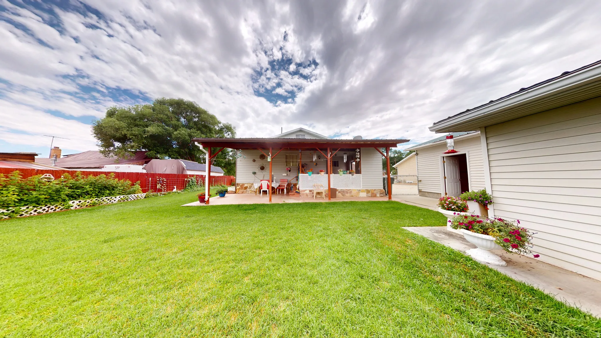 Expansive green lawn featuring a covered patio, paved patio flooring, and a red perimeter fence
