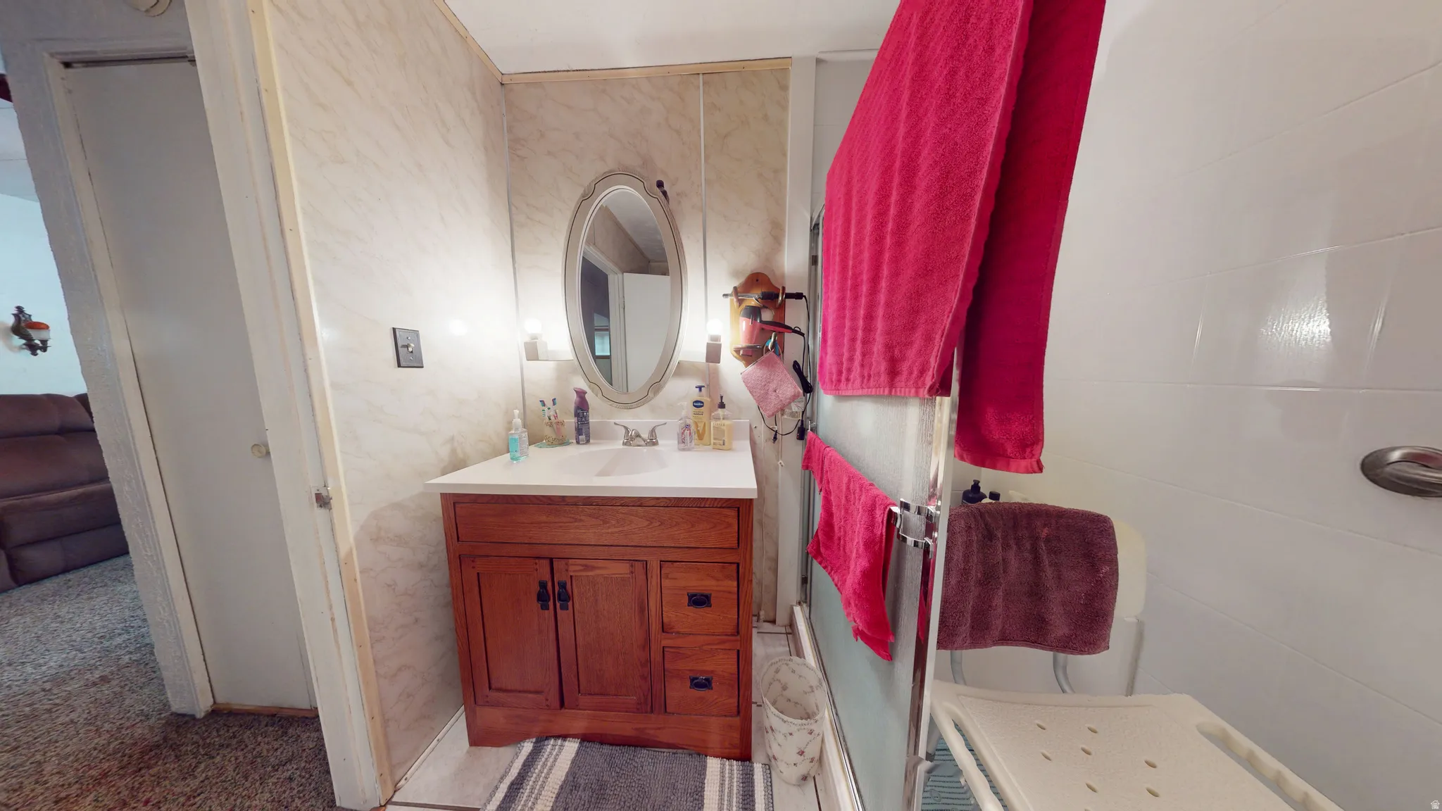 Bathroom featuring a wood-finish vanity with a white countertop and integrated sink, an oval wall-mounted mirror, and wall-mounted light fixtures
