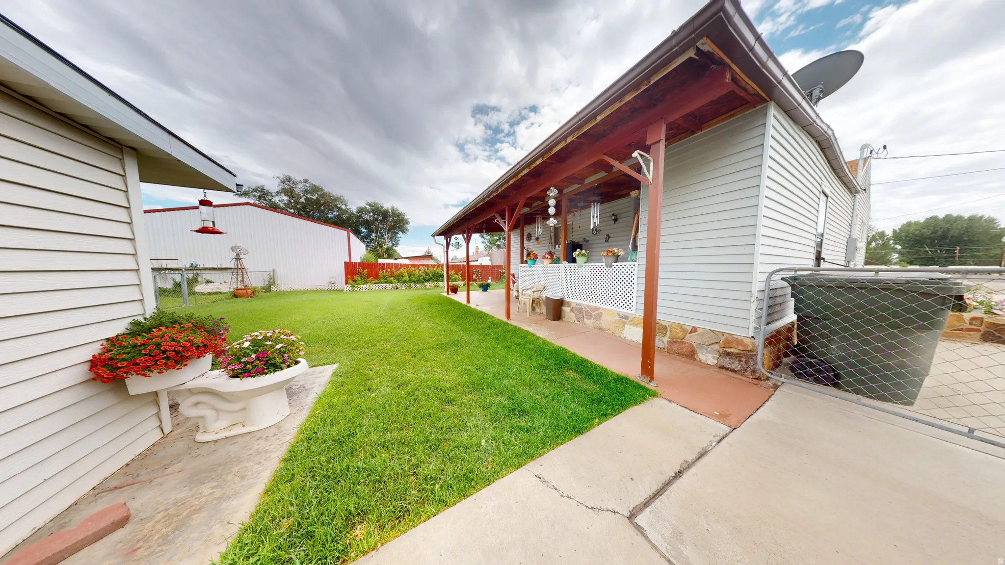 Expansive green lawn with a covered porch featuring wooden supports and a lattice railing